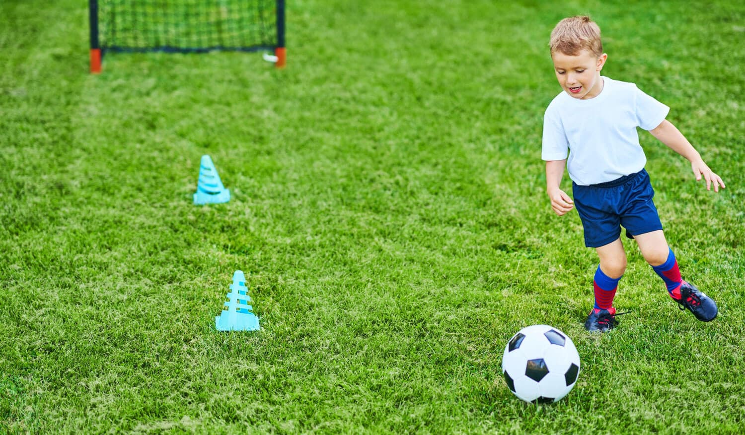 A young child dribbling a soccer ball on a grass field