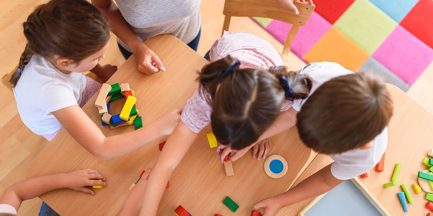 A teacher playing with children at a classroom table